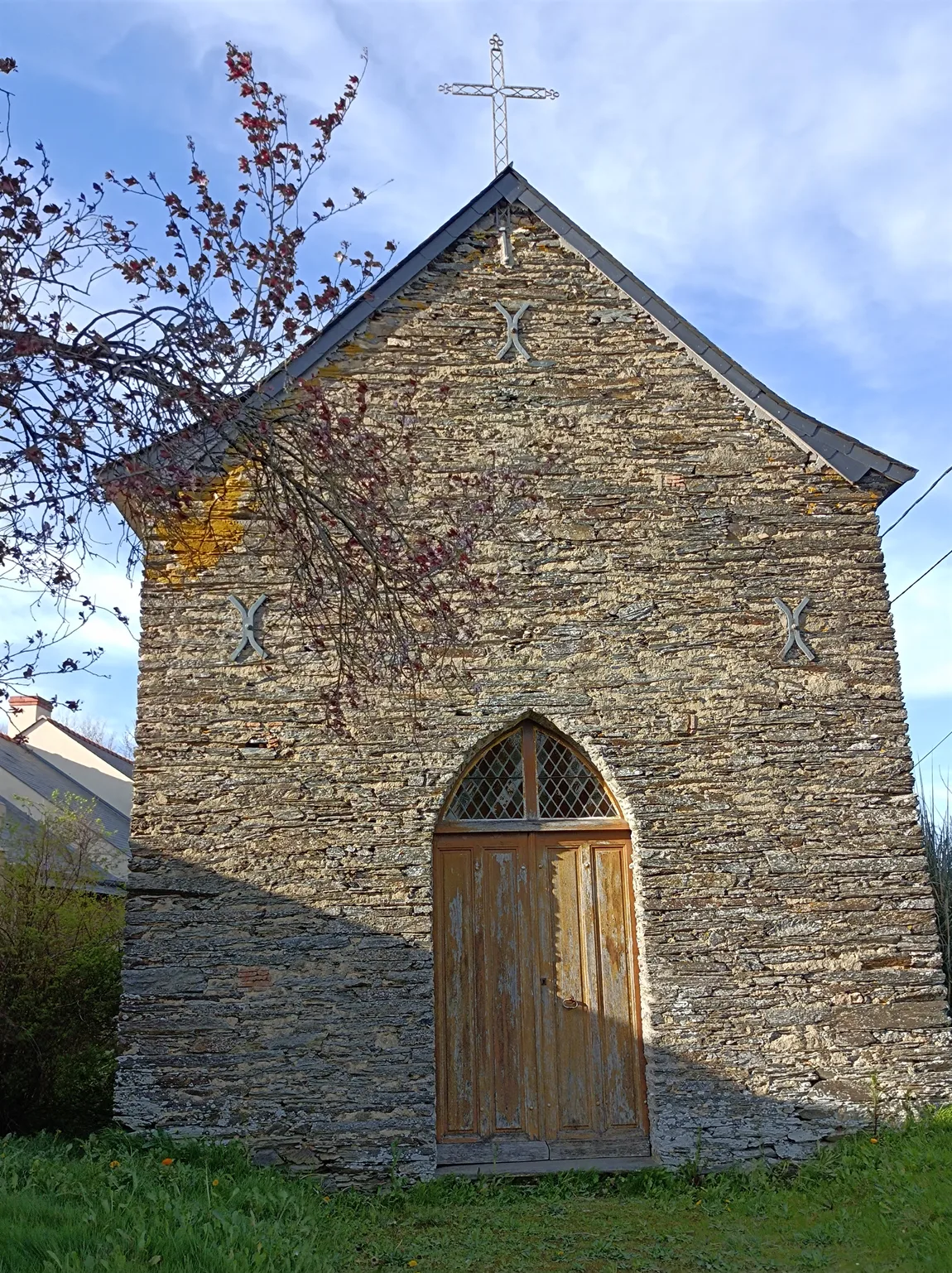 La façade de schiste de la chapelle du Rosaire de Freigné, couronnée d'une croix de fer, avec sa porte en arc brisé.