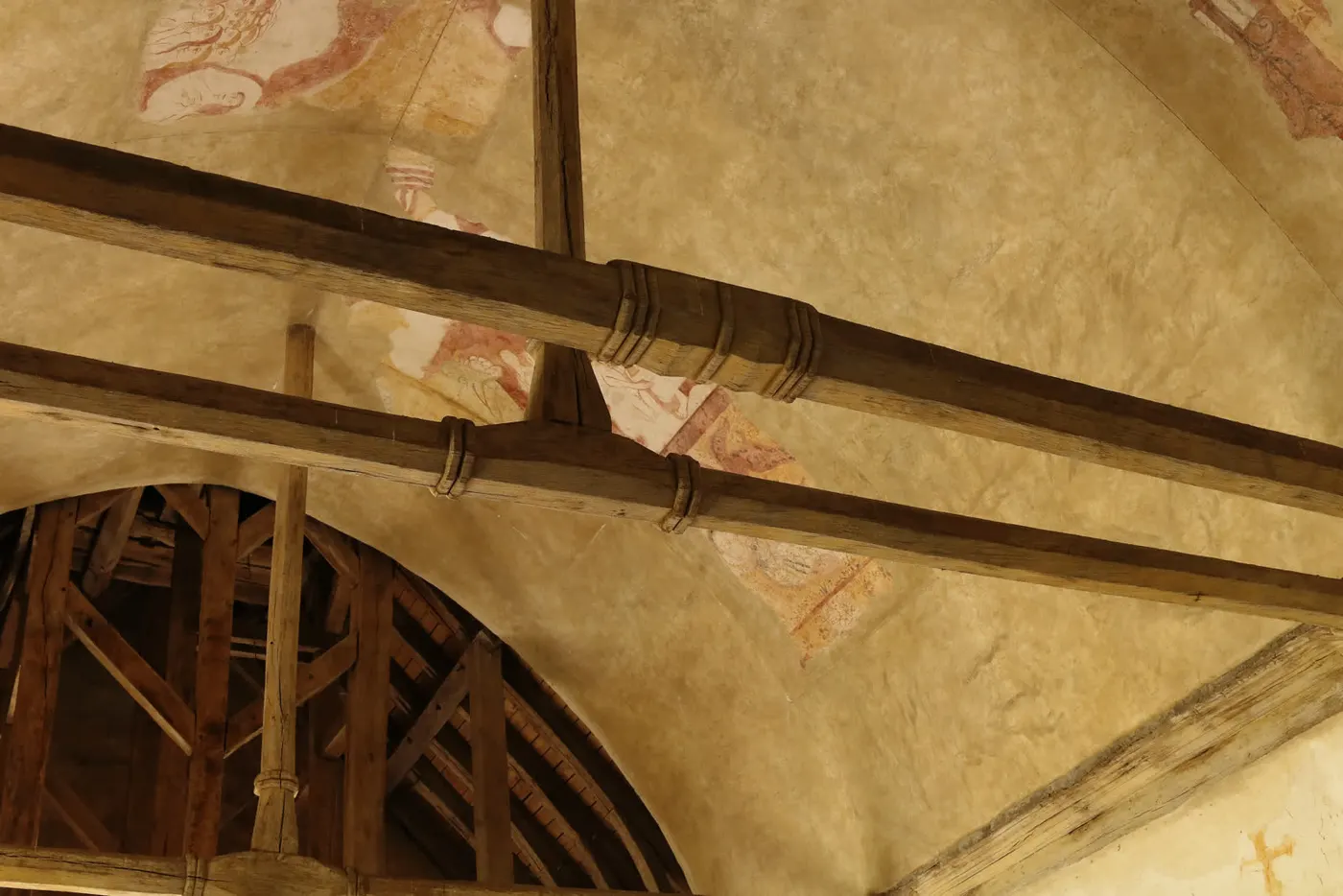 Les peintures murales du XVᵉ siècle de la chapelle du Vieux-Bourg, sous la charpente : ocres et rouges d'origine.